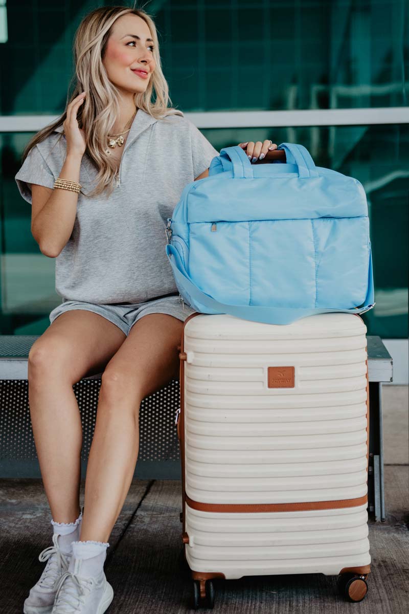 Light Blue Wholesale Weekender Bag w/ Pass-Thru Slip A woman traveling with a quilted blue weekender bag next to a piece of luggage