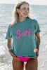 A woman standing on the beach wearing a teal surf tshirt