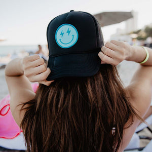woman on the beach wearing a black happy face trucker hat
