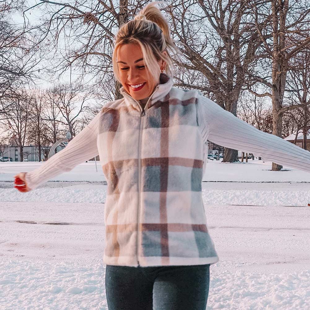 woman wearing leggings and a plaid vest standing outside in the snow