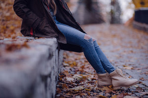 Woman in jeans, jacket, and boots sitting on a ledge surrounded by leaves
