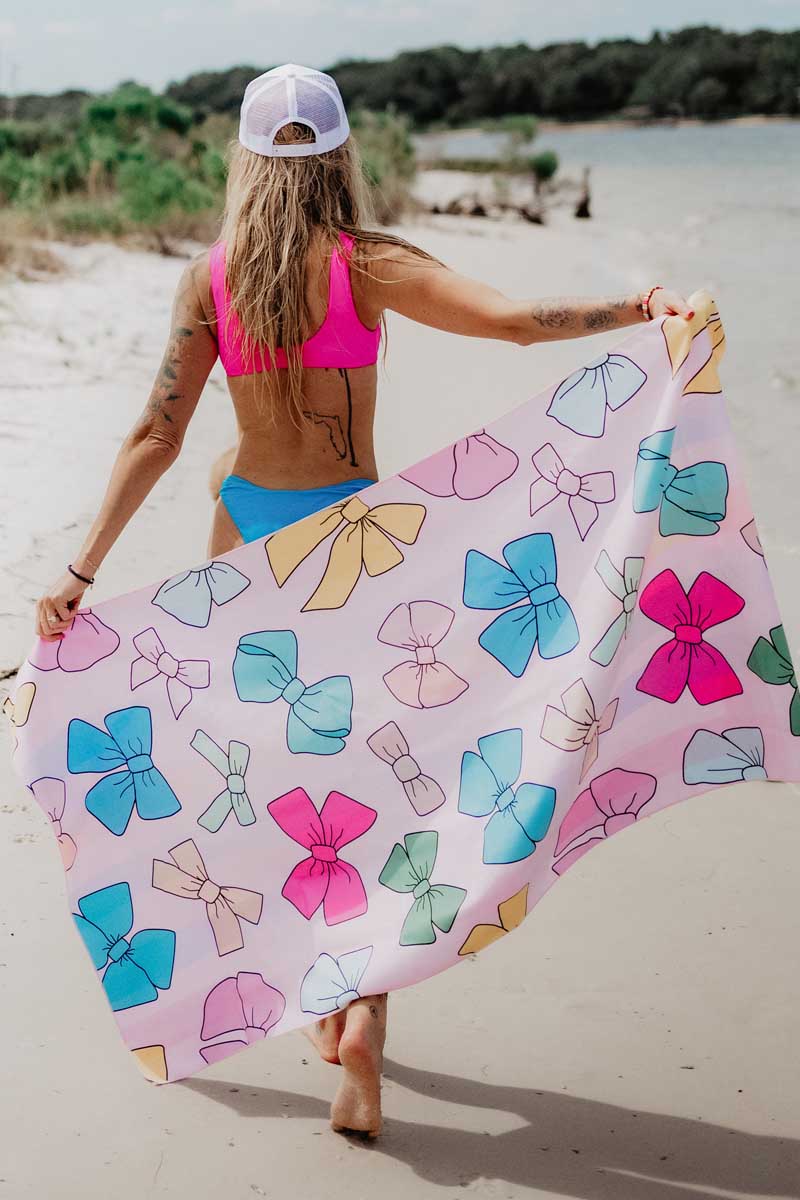A woman walking on a beach holding a pink bow pattern beach towel