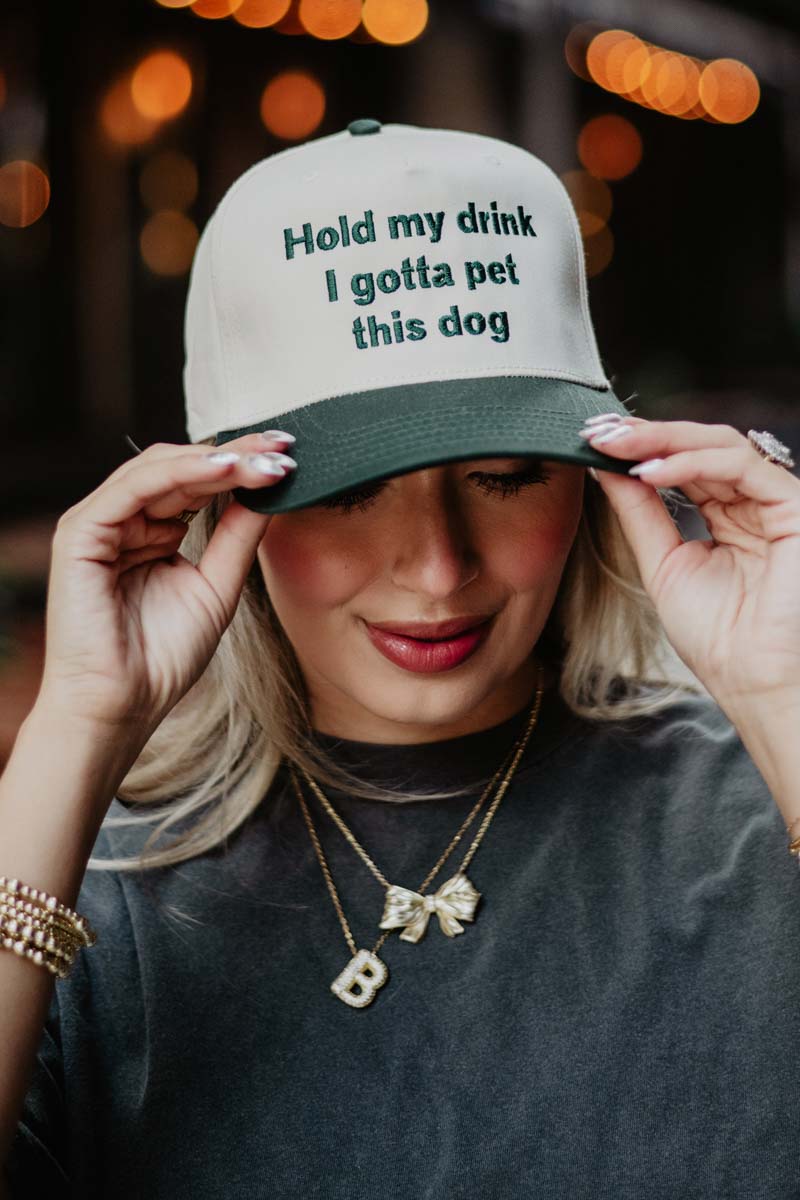 A woman wearing a pink and white two toned trucker hat that reads hold my drink I gotta pet this dog