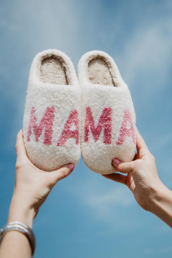 Two hands holding up a pair of slippers with mama written on them