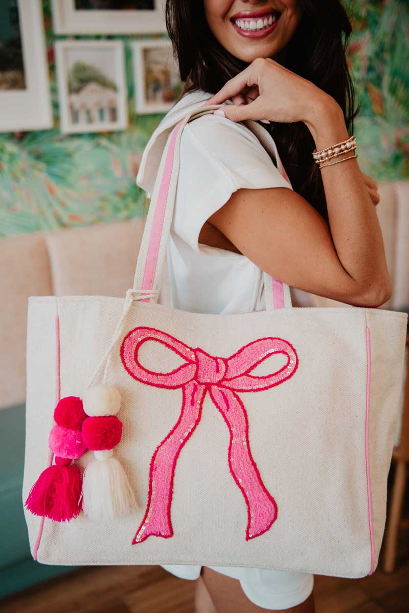 A woman holding a white tote with a pink bow design