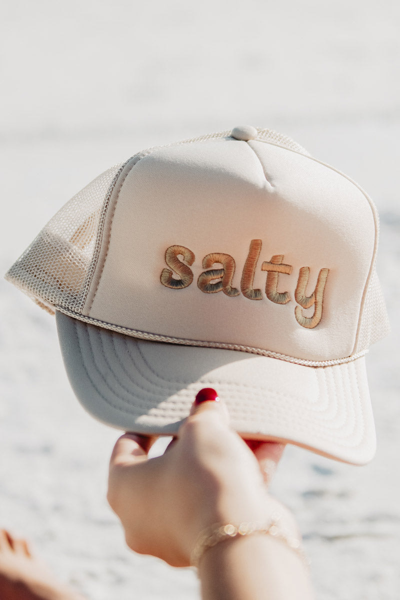 A woman holding a beige minimalist Salty trucker hat