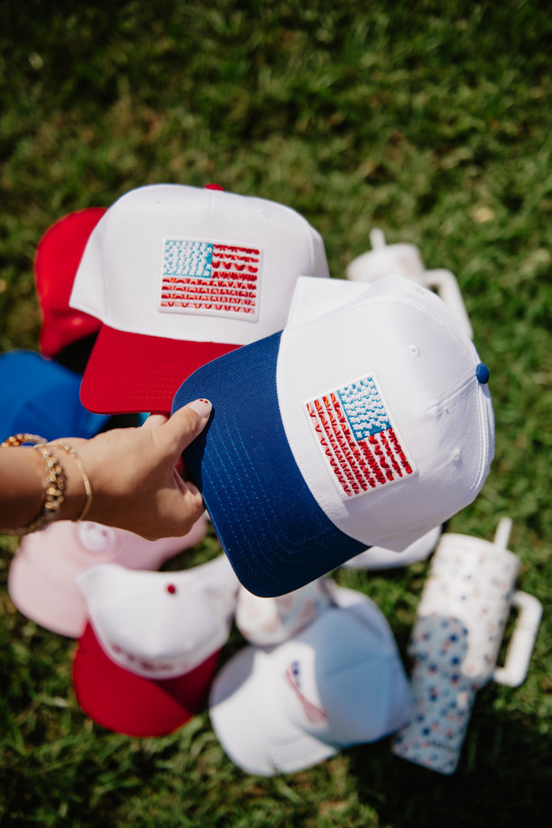 A woman holding two toned hats with an embroidered American flag