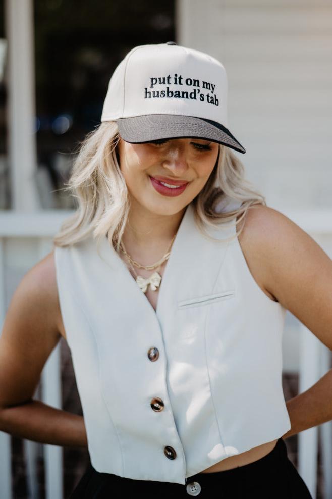 A woman wearing a trendy hat that says put it on my husband's tab